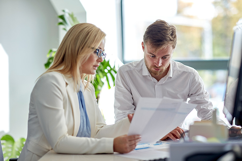 Mies ja nainen tutkimassa papereita tietokoneen ääressä